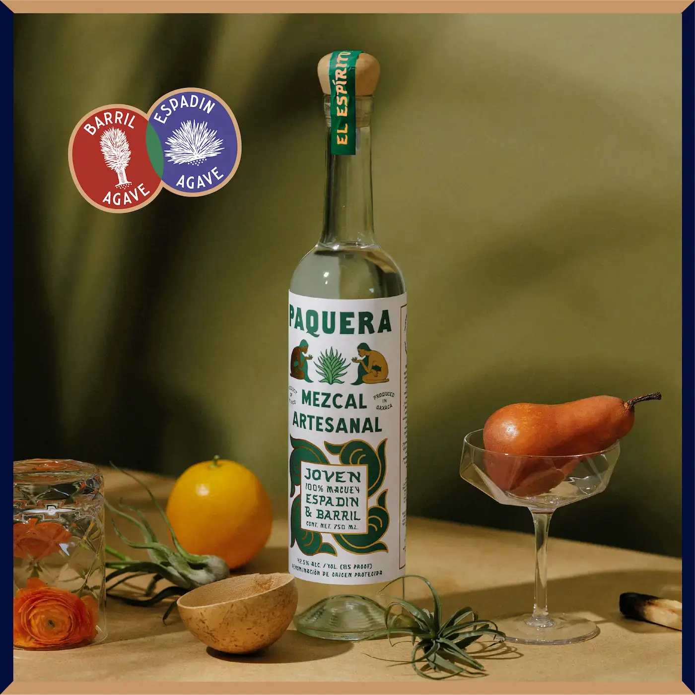 Paquera Mezcal Artesanal Espadín & Barril bottle set against an earthy green backdrop, styled with fresh fruit, botanicals, and artisanal elements.