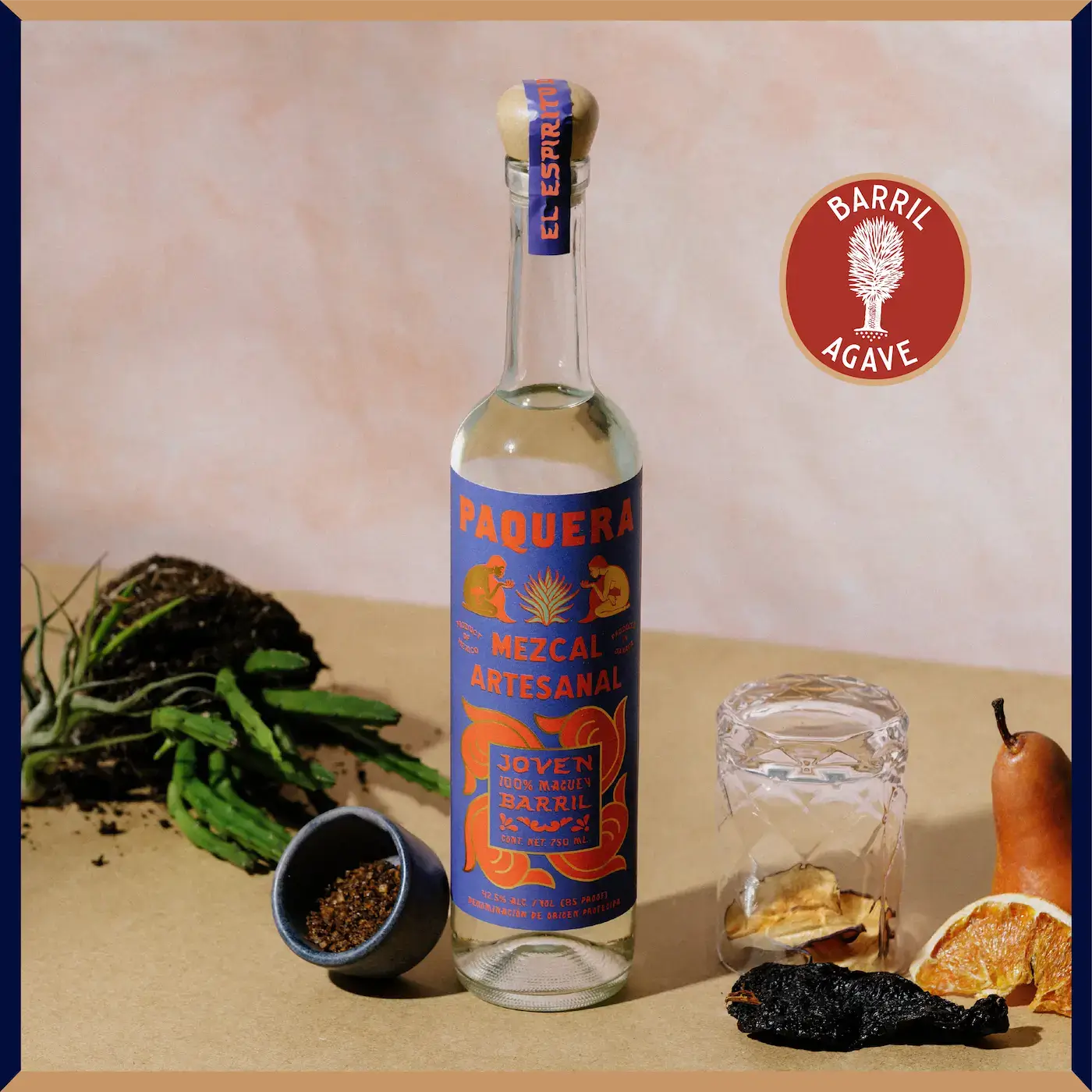 Paquera Mezcal Artesanal Barril bottle with a warm-toned background, styled with dried fruits, spices, and fresh agave.
